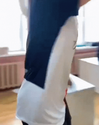 A Man In A Blue And White Shirt Is Standing In A Room With His Arms Outstretched . GIF