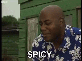 A Man In A Blue And White Shirt Says Spicy In Front Of A Green Building . GIF