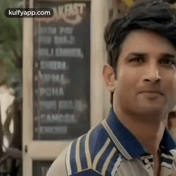 a man in a blue and white striped shirt is standing in front of a restaurant .