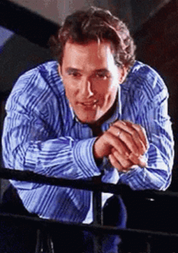 a man in a blue and white striped shirt leans on a railing
