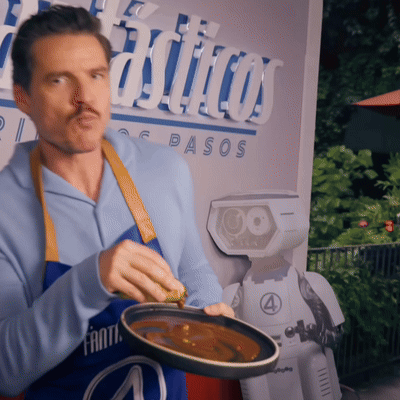 A Man In A Blue Apron Is Holding A Pan Of Food In Front Of A Sign That Says Pasos GIF
