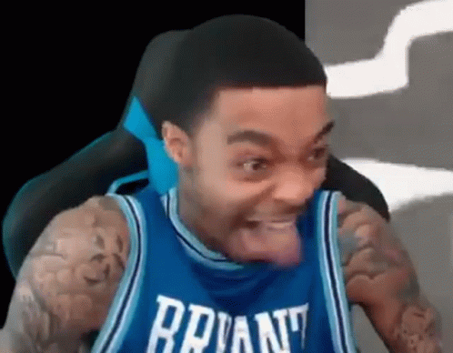 A Man In A Blue Basketball Jersey Is Sitting In A Chair With His Tongue Hanging Out . GIF