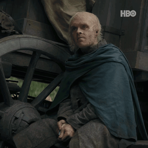 A Man In A Blue Cape Sits In Front Of A Wagon Wheel With The Hbo Logo On The Bottom GIF