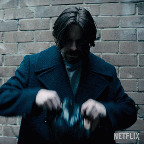 A Man In A Blue Coat Is Standing In Front Of A Brick Wall With A Netflix Logo Behind Him GIF
