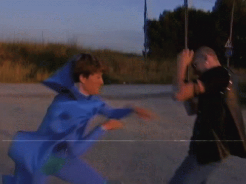 A Man In A Blue Costume Is Fighting Another Man In A Black Shirt GIF