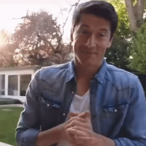 A Man In A Blue Denim Jacket Is Clapping His Hands . GIF