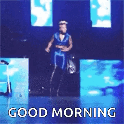 A Man In A Blue Dress Is Dancing On A Stage With The Words `` Good Morning '' Below Him . GIF