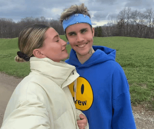 A Man In A Blue Drew Hoodie Kisses A Woman GIF