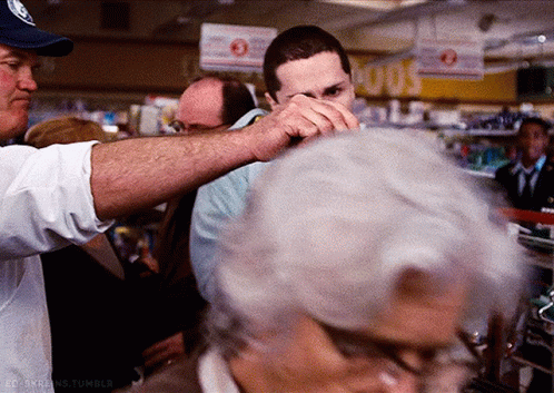 A Man In A Blue Hat Holds A Man 'S Hand Over His Face In A Store GIF