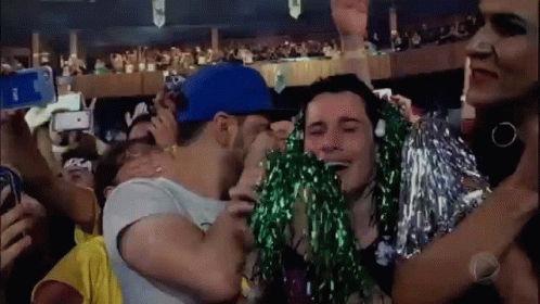 A Man In A Blue Hat Is Kissing A Woman In A Crowd . GIF