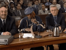 A Man In A Blue Hat Is Sitting At A Table With Other Men GIF