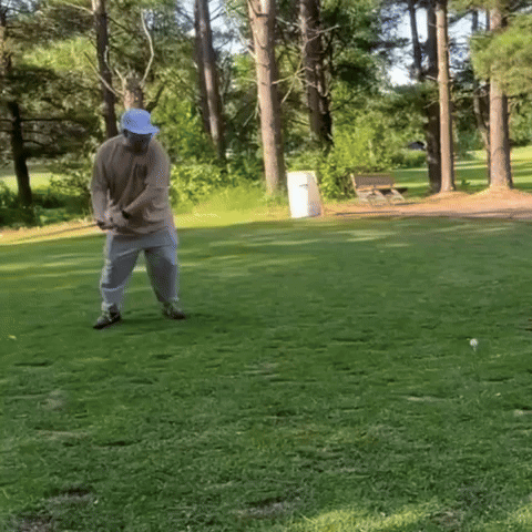 A Man In A Blue Hat Is Swinging A Golf Club On A Golf Course GIF