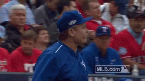 A Man In A Blue Hat Stands In Front Of A Mlb.com Logo GIF