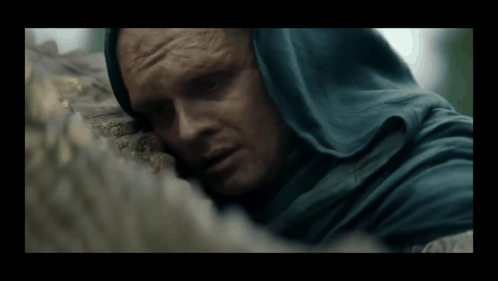 A Man In A Blue Hooded Cloak Is Laying On A Rock GIF