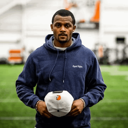 A Man In A Blue Hoodie Holds A White Baseball Cap GIF