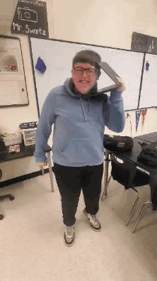 A Man In A Blue Hoodie Is Holding A Tablet Over His Shoulder In Front Of A White Board That Says Mr. Sweetz GIF