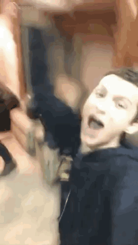A Man In A Blue Hoodie Is Making A Funny Face While Sitting On A Couch . GIF