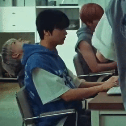 A Man In A Blue Hoodie Is Sitting In A Chair In Front Of A Computer . GIF
