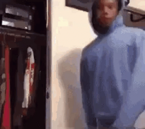 A Man In A Blue Hoodie Is Standing In Front Of A Closet With Clothes Hanging On It . GIF