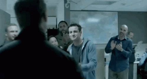 A Man In A Blue Hoodie Is Standing In Front Of A Group Of People Applauding . GIF