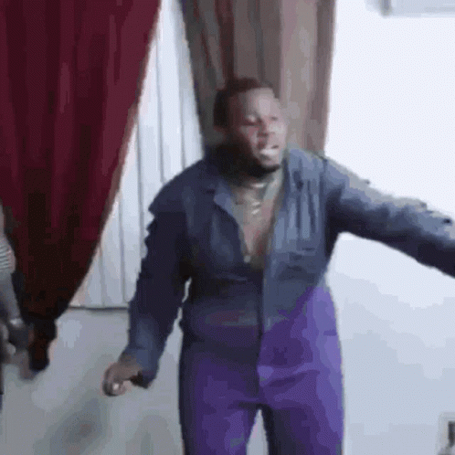 A Man In A Blue Jacket And Purple Pants Is Standing In A Room . GIF