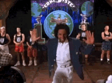 A Man In A Blue Jacket And White Pants Is Dancing On A Stage In Front Of A Crowd . GIF