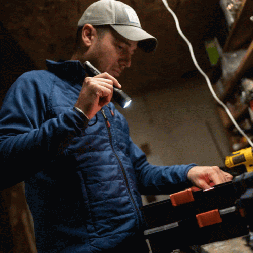 A Man In A Blue Jacket Holds A Flashlight In His Hand GIF