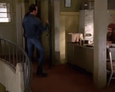 A Man In A Blue Jacket Is Dancing In A Room With A Spiral Staircase GIF