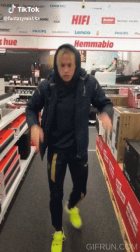 A Man In A Blue Jacket Is Dancing In A Store With A Sign That Says Hifi GIF