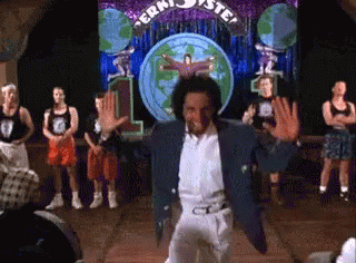 A Man In A Blue Jacket Is Dancing In Front Of A Sign That Says ' Jerk ' GIF