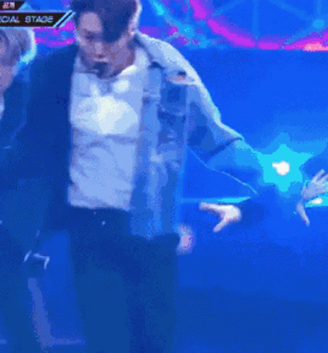 A Man In A Blue Jacket Is Dancing In Front Of A Special Stage Banner GIF