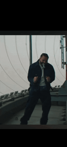 A Man In A Blue Jacket Is Dancing In Front Of A Window GIF
