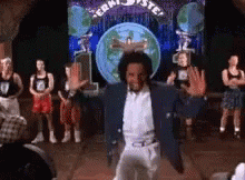 A Man In A Blue Jacket Is Dancing On A Stage In Front Of A Crowd Of People . GIF