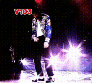 A Man In A Blue Jacket Is Dancing On A Stage In Front Of A Sign That Says " V103 " GIF