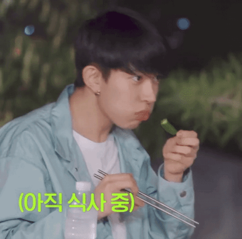 A Man In A Blue Jacket Is Eating Something With Chopsticks And A Bottle Of Water GIF