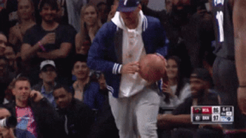 A Man In A Blue Jacket Is Holding A Basketball In Front Of A Crowd Of People GIF