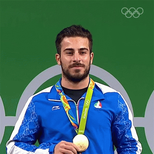 A Man In A Blue Jacket Is Holding A Gold Medal From The Olympics GIF