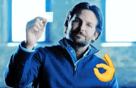 A Man In A Blue Jacket Is Holding A Piece Of Paper In His Hand And Making An Ok Sign . GIF