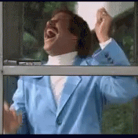 A Man In A Blue Jacket Is Laughing While Looking Out A Window . GIF