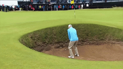 A Man In A Blue Jacket Is Playing Golf In A Bunker GIF