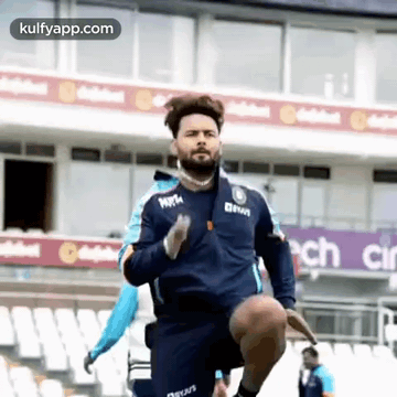 A Man In A Blue Jacket Is Running On A Stadium . GIF