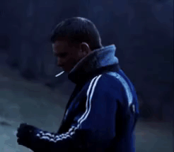 a man in a blue jacket is smoking a cigarette while standing in the dark .