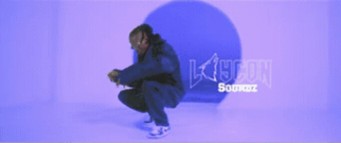 A Man In A Blue Jacket Is Squatting Down In Front Of A Purple Background That Says K19con GIF