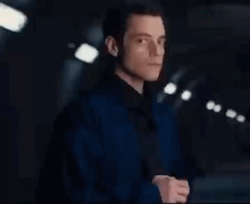 A Man In A Blue Jacket Is Standing In A Dark Room . GIF