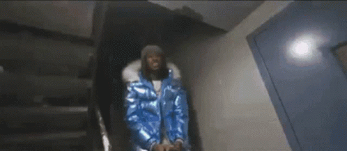 A Man In A Blue Jacket Is Standing In A Dark Room . GIF