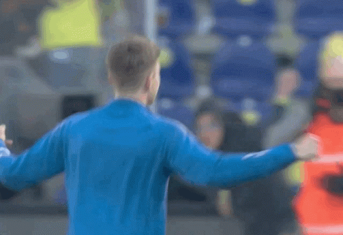 A Man In A Blue Jacket Is Standing In Front Of A Crowd With His Fist In The Air GIF
