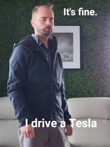 A Man In A Blue Jacket Is Standing In Front Of A Picture That Says I Drive A Tesla GIF