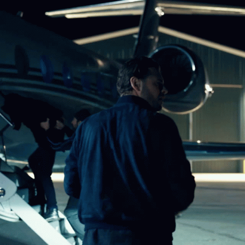 A Man In A Blue Jacket Is Standing In Front Of A Plane With The Letters Aa On The Tail GIF