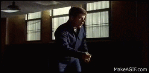 A Man In A Blue Jacket Is Standing In Front Of A Window In A Room . GIF