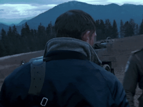 a man in a blue jacket is standing in front of mountains